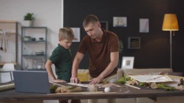 Yetişkin beyaz bir adamın, oğluyla birlikte renkli uçan uçurtma yaparken orta boy el resmi.