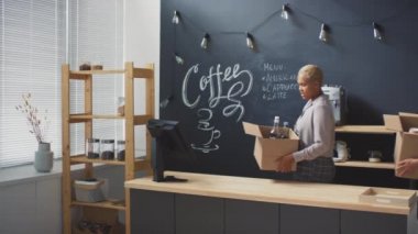 İki çoklu etnik içerikli kahve dükkanı çalışanının elinde envanter kutuları, küçük kasalarda sohbet ederken, raflarda kavanoz ve kağıt bardakları düzenlerken, kafeteryayı açmak için hazırlarken orta halli bir fotoğrafı.