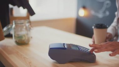 Tanımlanamayan bir kadının, kahve dükkanından kahve alırken görüntüsü. Ulaşılamayan işlemler için akıllı telefonu terminale bağlıyor.