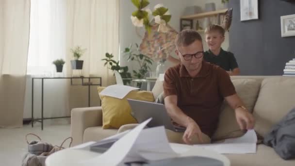 Babası Laptopla Kağıtları Gözden Geçirmeye Çalışırken Oturma Odasında Uçan Kağıt — Stok video