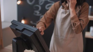 Küçük kapalı kafeteryada çalışan Asyalı bir kadının kasada yazarken telefonla konuştuğu yavaş çekimde yakın plan çekimler.