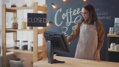 Orta ölçekli, Asyalı önlüklü genç bir kadının kasada durup tabelayı açtığı ve kameraya gülümsediği görüntüler.