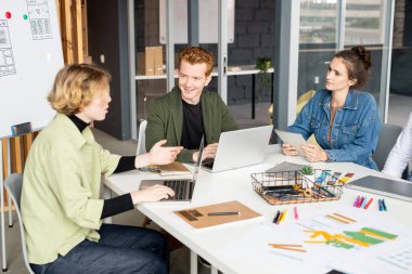 Genç ve mutlu erkek mobil uygulama geliştiricisi beyin fırtınası ve yaratıcı fikirler tartışması sırasında bayan meslektaşlarından birine bakıyor.