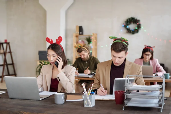 年轻的当代跨文化同事 穿着时髦的便服 头戴圣诞头巾 成排坐在手提电脑前结成网络 — 图库照片