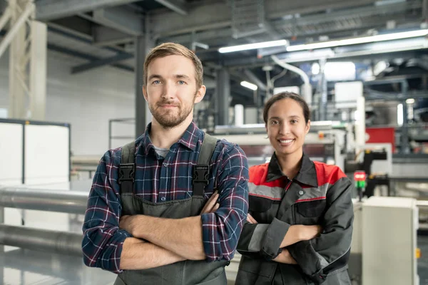 两个年轻的成功的聚合体加工厂工人站在大车间的摄像机前 两手叉腰 两臂交叉 — 图库照片