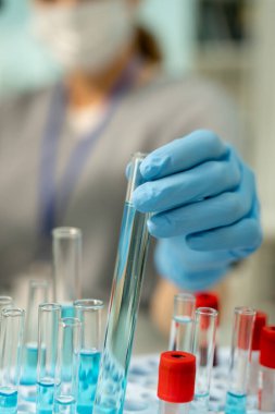 Çağdaş kadın klinikçinin eldivenli eli ya da tıbbi laboratuvar çalışanı test etmeden önce yeni aşı örneğiyle birlikte matara alıyor.