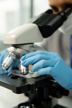 Kimyasal örnekleri araştırmaya giderken mikroskobun metalik merceğini tamir eden bilimsel laboratuvar çalışanı ya da araştırmacısının eldivenli eli