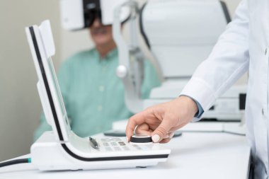 Çağdaş kadın göz doktorunun eli, kıdemli bir adamın görüşünü incelerken aletin düğmesini çeviriyor.