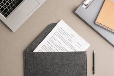 Dizüstü bilgisayarla çevrili büyük gri zarf içinde mali sözleşmenin genel görünümü, dokümanlı dosya ve işyeriyle ilgili telif defteri