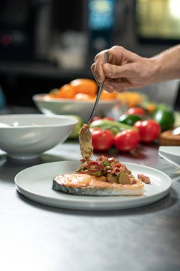 Erkek aşçı sıcak iştah açıcı sebze yahnisini bir parça kızarmış somonla birlikte restoranın müşterisi için lezzetli bir yemek hazırlıyor.