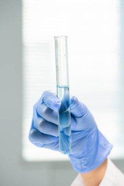 Laboratuvardaki bilimsel deney sırasında kameranın önünde saf su dolu matarayı tutan çağdaş genç araştırmacının eldivenli eli.