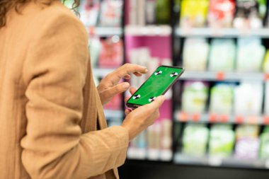 Genç ve çağdaş kadın tüketicinin elleri ekranın önünde güzellik ürünleriyle birlikte yeşil e-kuponlu akıllı telefon kullanıyor.