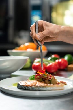 Erkek şefin eli, müşteriye yemek hazırlarken iştah açıcı sebze güvecinin üzerine bir parça kızarmış somon koyuyor.