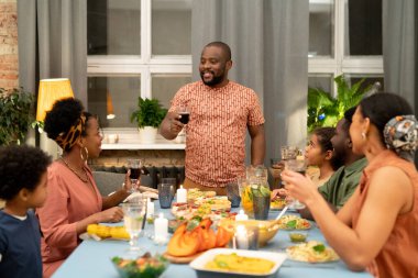 İçkili büyük bir aile ellerinde kırmızı şarapla mutlu babaya bakıyor bayram masasının yanında duruyor ve tost yapıyorlar.