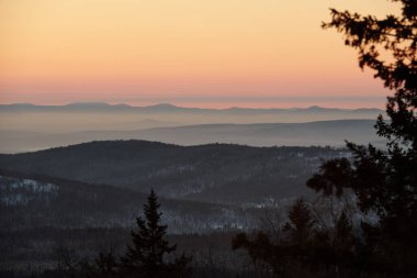 Kış akşamında doğanın muhteşem manzarası. Uzun dağ zincirleri ve gün batımında pembe gökyüzü ile karışık ormanlar.