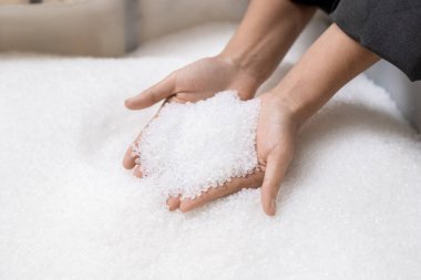 Çağdaş polimer işleme fabrikasının genç bayan işçisinin elleri işlenmemiş beyaz plastik topaklar tutuyor.