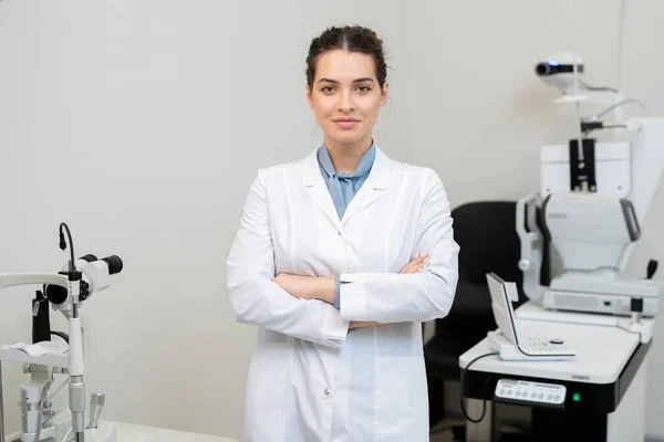 Jovem Morena Sorridente Oftalmologista Whitecoat Cruzando Braços Pelo Peito Enquanto — Fotografia de Stock