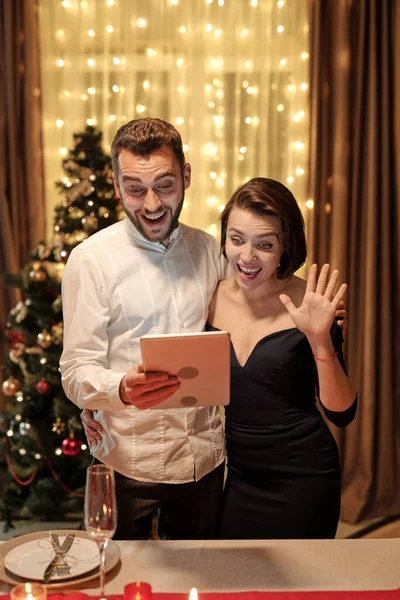 年轻貌美的夫妻一边看智能手机屏幕 一边在视频聊天中与人交流 妻子挥手 — 图库照片
