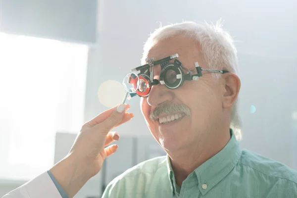 笑顔シニア男座っていますで眼科医の前で彼の視力の医療検査中に彼の視力とともに観光試験フレームで現代のクリニック — ストック写真