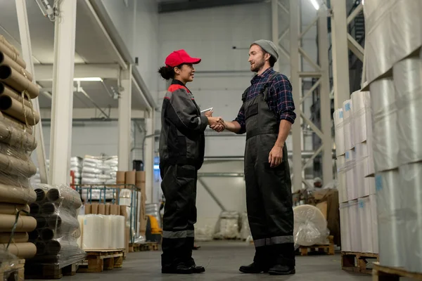 在仓库工作期间 身穿工作服和格子衬衫的年轻男性专业人员与他的女同事用数码平板电脑握手 — 图库照片