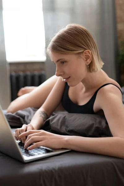 幸せなブロンド女の子でLeotardサーフィンでネット上で横になっている間にベッドの上で寝るとオンラインビデオをスクロールしたり 彼女の新しい写真を投稿 — ストック写真