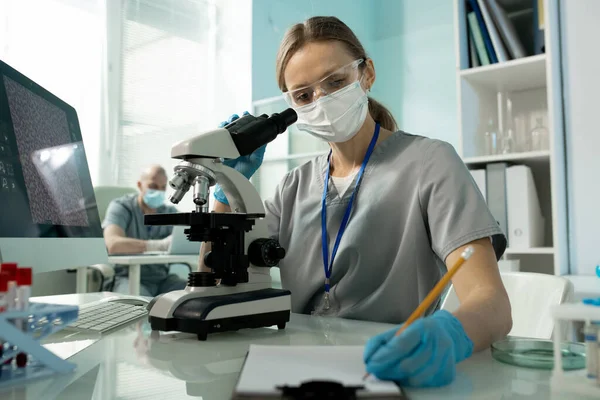 Jovem Trabalhadora Laboratório Uniforme Máscara Protetora Luvas Óculos Fazendo Anotações — Fotografia de Stock