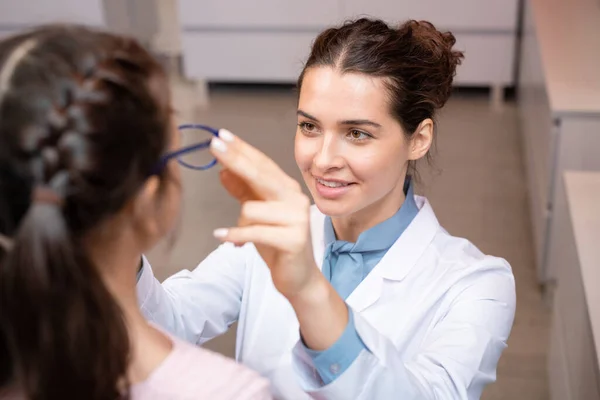 幸せな若いです女性眼科医でホワイトコート置くペアの新しい眼鏡上の顔の可愛いです女の子後に彼女の視力のチェックアップ — ストック写真