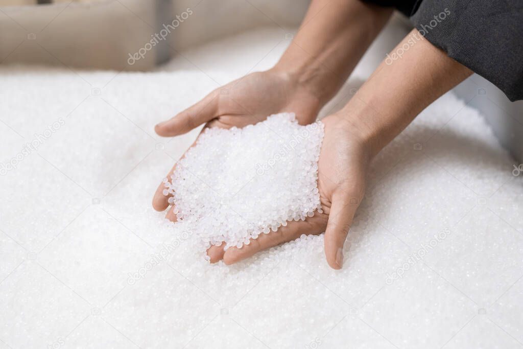 Hands of young female worker of large contemporary polymer processing factory holding pile of unprocessed white plastic pellets