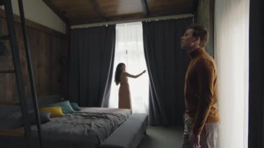 Lüks otel odasında perdeleri açan akıllı Asyalı kadının erkek arkadaşıyla birlikte pencereden dışarı bakarken çekilmiş yavaş çekimleri.