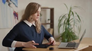 Genç kadın ressamın dijital çizim masasında nasıl çizileceğini öğretirken çekilmiş orta boy bir fotoğraf. Bilgisayarla içeride masa başında otururken.