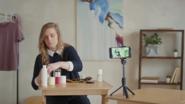 ウエストアップ映像のCaucasian女性座っていますにデスクレコーディングビデオの作り方について自宅の洗濯ブラシでマイクロセラー水を使用して — ストック動画