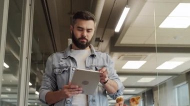 Düşük açılı, belden aşağısı karışık bir ofis çalışanı dijital tabletle geniş çağdaş ofise bakıyor.