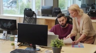 İki yetişkin çok ırklı iş adamının basılı raporu tartışırken, modern açık uzay ofisinde çalışırken orta boy fotoğrafı.