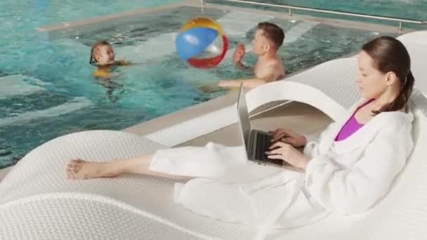 慢动作全速拍摄的高加索家庭一起呆在屋顶热水池里 女人躺在笔记本电脑上 父亲和小女孩与海滩球一起游泳 — 图库视频影像