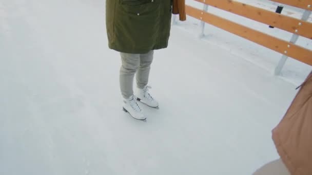 ハンドヘルド追跡中アップの美しいです女性で冬服取りますスケートレッスンともに彼女のボーイフレンドティーチングとともにアイスリンク屋外で — ストック動画