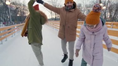 Üç kişilik mutlu bir ailenin buz pateni pistinde dans ederken, gülümseyen bir adamın karısını ve kızını dans ettirirken orta yavaş çekimleri.
