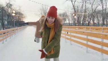 Genç ve neşeli bir ailenin kışın buz pateni pistinde buz pateni yaparken eğlenirken yavaş çekim görüntülerini izliyoruz.