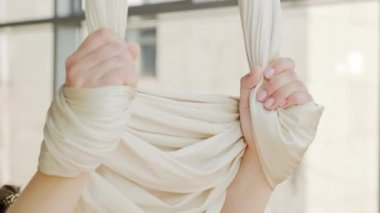 Kafkasyalı genç bir kadının yakın çekimleri, esneme hareketleri, öne eğilmeleri, parlak yoga stüdyosunda hava hamakları tutmaları.