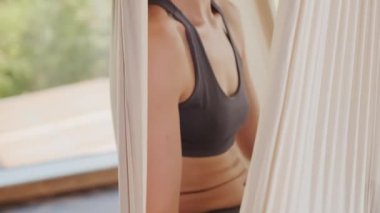 Nilüfer çiçeği pozunda meditasyon yapan genç beyaz kızın yakın plan portresi asılı hamakta oturuyor ve kameraya bakıp gülümsüyor.