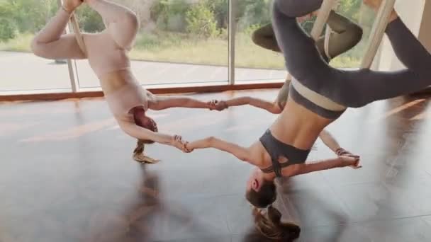 手持式拍摄的3名运动女子倒挂在瑜伽吊索上手牵手旋转练习瑜伽 — 图库视频影像