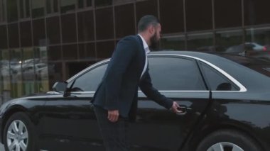 Orta ölçekte başarılı bir karma yarış işkadını pahalı siyah bir arabanın arka koltuğundan iniyor ve takım elbiseli bir erkek sürücü onun için kapıyı açıyor.