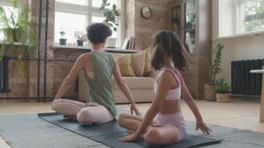 Spor kıyafetli anne ve küçük kızın yavaş yavaş yoga minderinde poz vermeleri ve sırtlarını esnetmeleri.