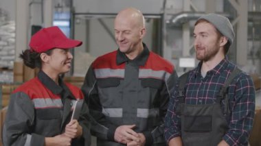 Yavaş çekimde, polietilen fabrikasında konuşan ve gülümseyen kameraya bakan çok ırklı işçilerin belden yukarı portresi.