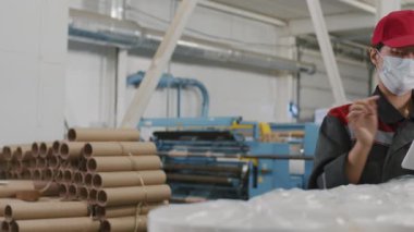 Tek kullanımlık koruyucu maskeli kadın fabrika işçisinin yavaş çekim görüntülerini tarıyorum. Üretilen polietilen kalitesine dokunarak ve dijital tablet üzerine notlar alarak kontrol ediyorum.