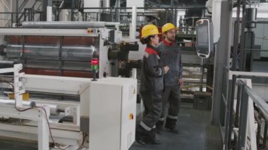 Endüstriyel fabrikada çalışan birkaç mühendisin modern makine ekipmanlarını tartıştığı orta ölçekli yavaş çekim görüntüleri.