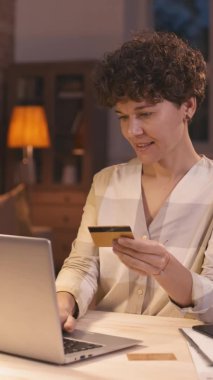 İnternetten alışveriş yapan neşeli bir kadının dikey çekimi. İnternetten sipariş veriyor ve alışverişi kutluyor.