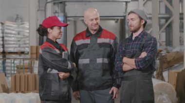 Polietilen fabrikasında kameraya bakan, çok ırklı, güler yüzlü, tulumlu üç fabrika işçisinin orta yavaş çekim görüntüleri.