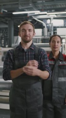 Profesyonel fabrika işçilerinin dikey yavaş portresi. Üniformalı işçilerin elleri bağlı kameraya bakmaları.