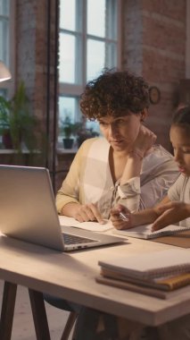 Kısa kıvırcık saçlı ve küçük kızı evde oturmuş öğretmeniyle videoda konuşurken PAN dikey pozu.