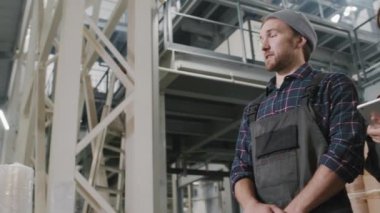 Dijital tablet ekranındaki bilgilere bakarak polietilen üretimini tartışan çok ırklı kadın ve erkek fabrika işçilerinin düşük açılı yavaş çekim görüntüsü.